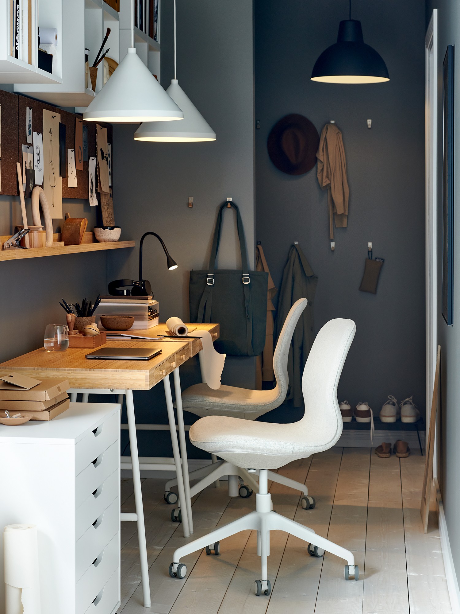 Narrow creative workspace with two compact desks, white chairs, wall storage and pendant lighting